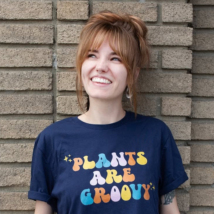 Person wearing a t-shirt with 'Plants Are Groovy' text standing against a brick wall.